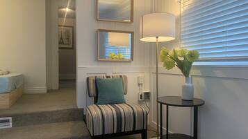A room with a striped chair, a small table with a vase of flowers, and a lamp.