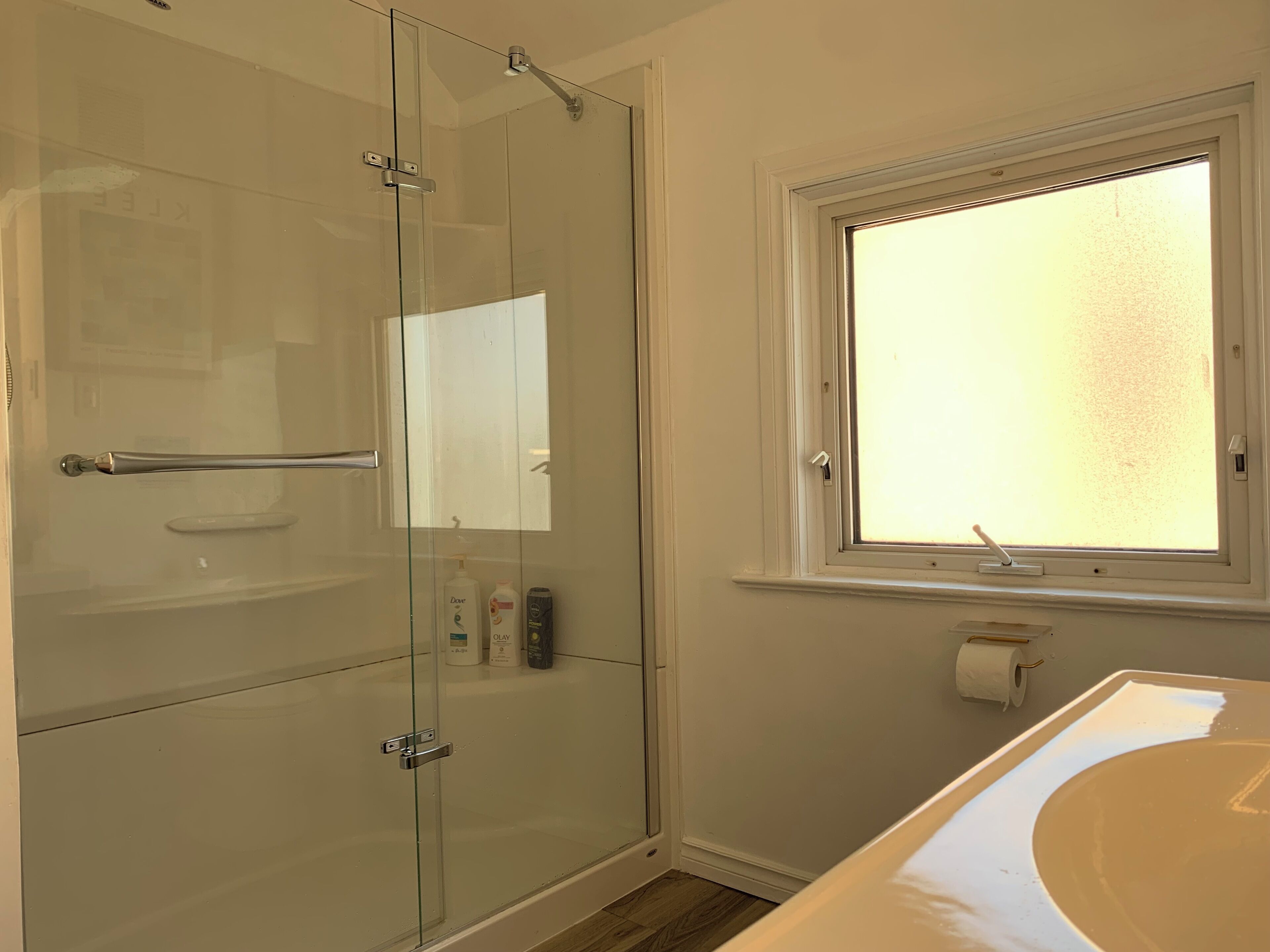 A bathroom with a glass-enclosed shower, a white sink, and a window.