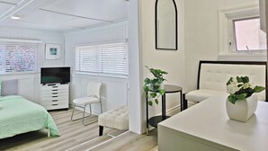 A bedroom with a bed, a chair, a bedside table, a mirror, and a window. - Winnipeg Holiday (Winnipeg)
