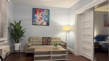 Ein Wohnzimmer mit einem beigen Sofa, einem Couchtisch, einer Zimmerpflanze, einem Bild an der Wand und einer Stehlampe.