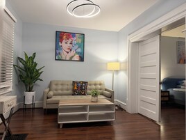 Una sala de estar con un sofá color beige, una mesa de centro, una planta en maceta, un cuadro en la pared y una lámpara de pie.
