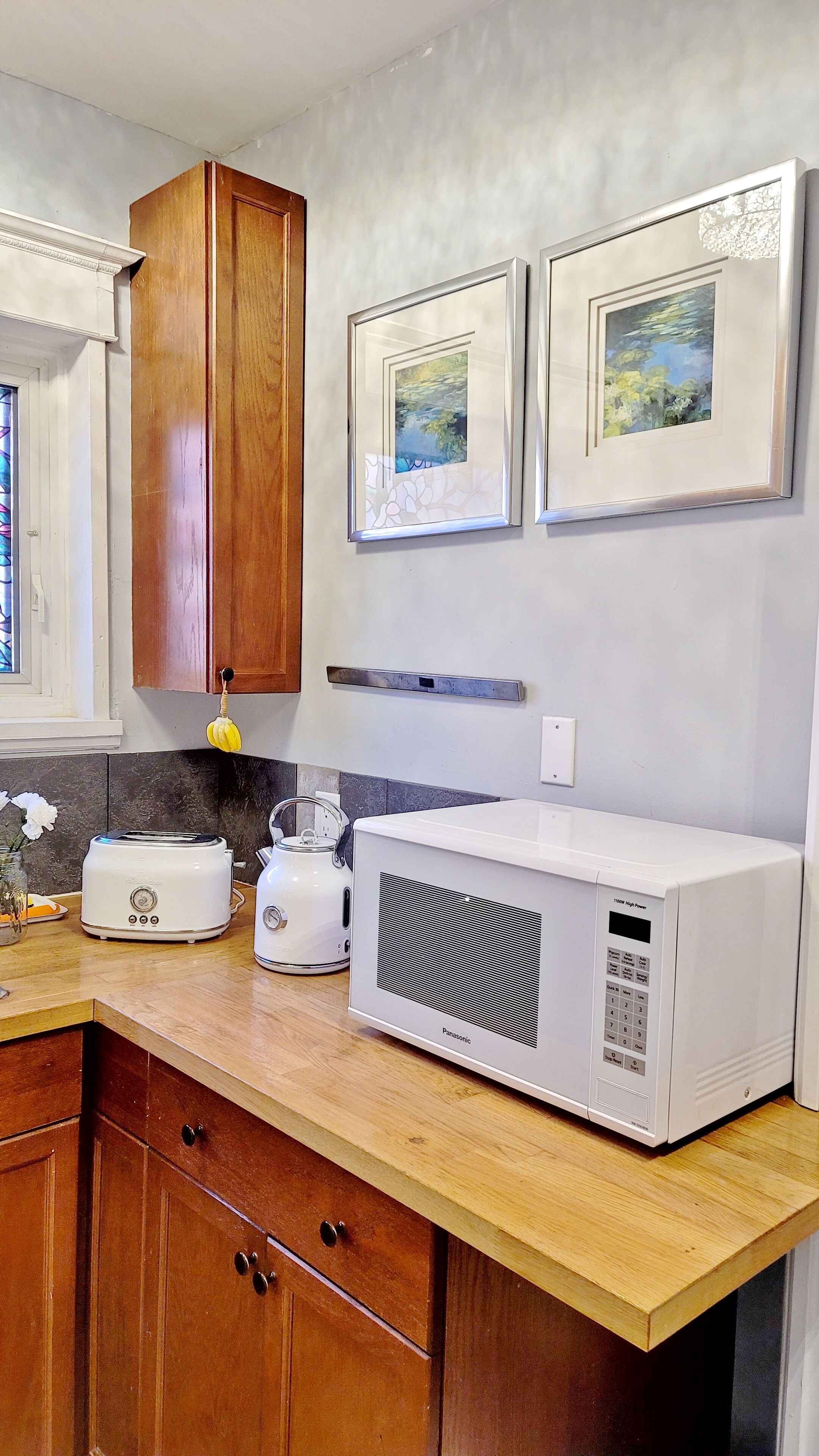 A kitchen with wooden cabinets, a toaster, a kettle, and a microwave. There are two framed pictures on the wall.