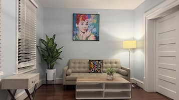 Ein Wohnzimmer mit einem beigen Sofa, einem Couchtisch, einer Zimmerpflanze, einem Bild an der Wand und einer Lampe.