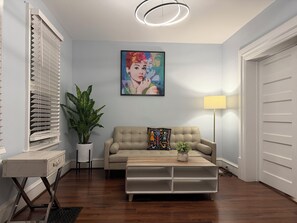 A living room with a beige sofa, a coffee table, a potted plant, a painting on the wall, and a lamp. - Winnipeg Holiday (Winnipeg)