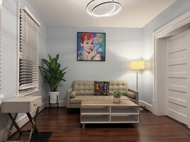Una sala de estar con un sofá color beige, una mesita de centro, una planta en maceta, un cuadro en la pared y una lámpara.