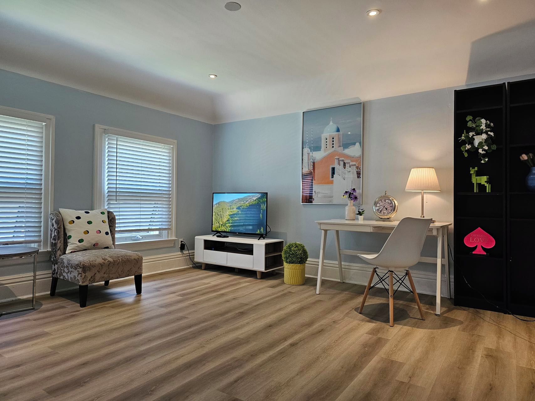 A living room with a television, a dining table, a chair, a lamp, and a bookshelf.