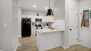 A modern kitchen with white cabinets, a black refrigerator, a microwave, and a hanging pendant light. - Near Park Circle, Downtown, & Beaches | Pool Table (Hanahan)