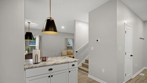 A modern kitchen with white cabinets, a marble countertop, and a black pendant light. - Near Park Circle, Downtown, & Beaches | Pool Table (Hanahan)