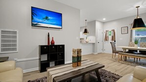A modern living room with a flat-screen TV, a dining area with a table and chairs, and a large window with curtains. - Near Park Circle, Downtown, & Beaches | Pool Table (Hanahan)