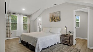 A bedroom with a large bed, a nightstand, a wall-mounted lamp, and a painting. - Near Park Circle, Downtown, & Beaches | Pool Table (Hanahan)