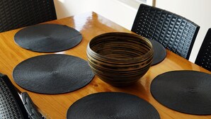 Una mesa de comedor de madera con individuales negros y un cuenco tejido en el centro.