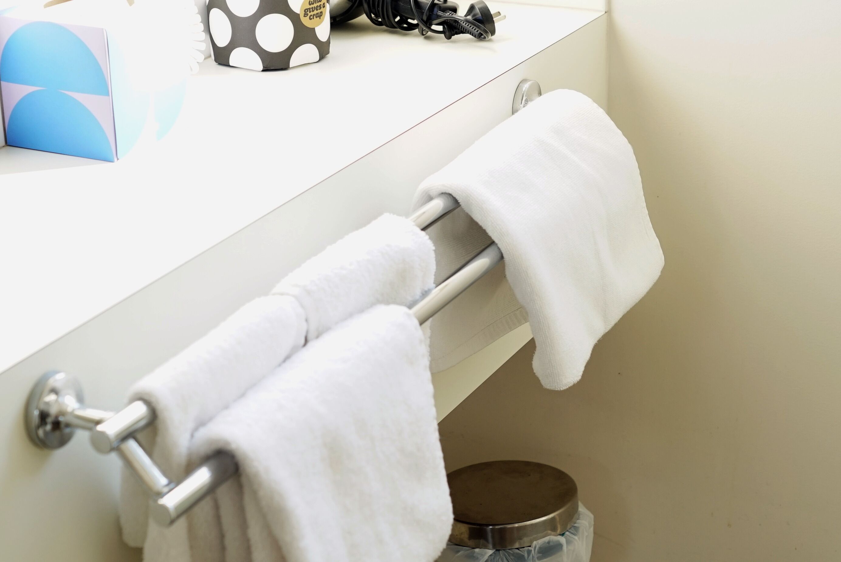 A bathroom with a white towel rack holding two towels, a trash bin, and a blue box with a geometric design.