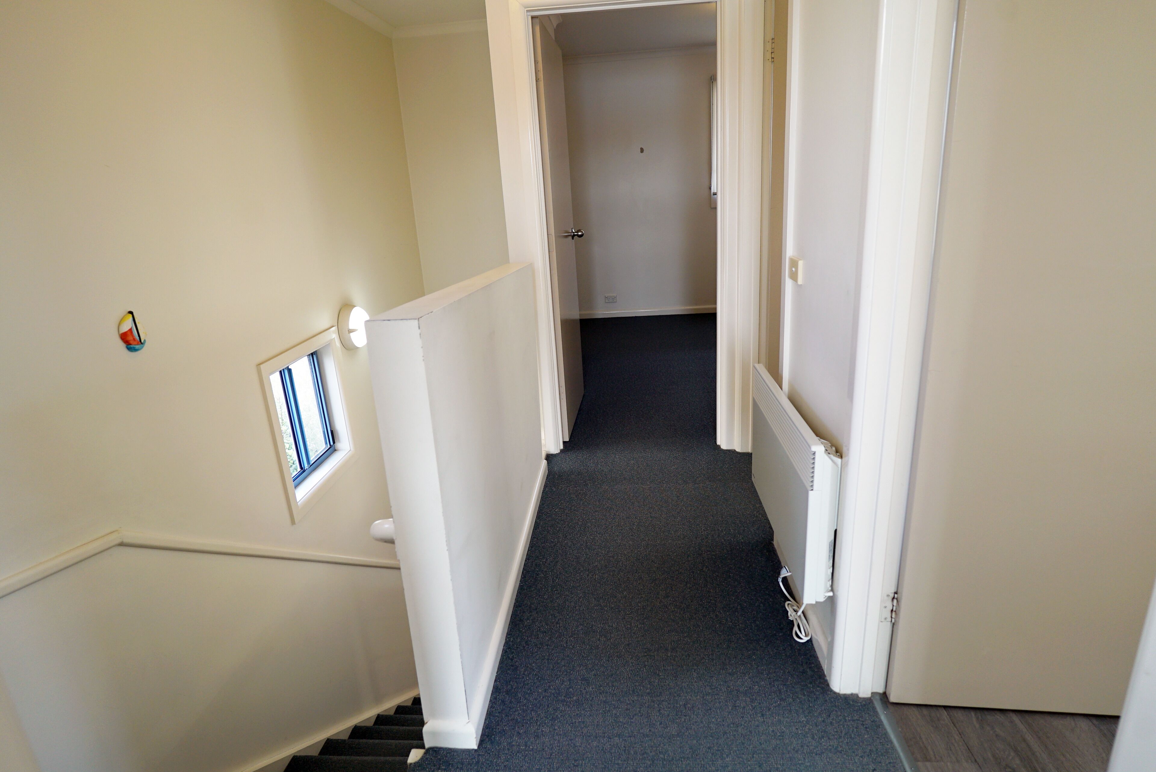 Un couloir étroit, doté d’un sol recouvert de moquette, de murs blancs et d’une porte au fond.