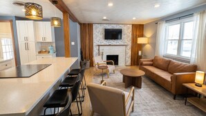 A modern living room with a fireplace, a sofa, a coffee table, and a dining area with chairs. - Guest Favorite- Denver Getaway Gem with Grill, Corn Hole, Basketball Court (Denver)