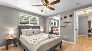 A bedroom with a bed, bedside lamps, a ceiling fan, a window, and a door leading to another room. - Guest Favorite- Denver Getaway Gem with Grill, Corn Hole, Basketball Court (Denver)