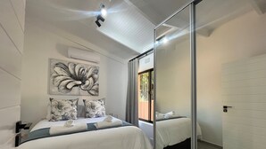 A modern bedroom with a large mirror, a ceiling fan, and a floral artwork on the wall.