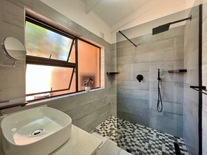 A bathroom with a large window, a sink, and a shower area.