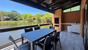 A patio with a table and chairs overlooking a body of water, a grill, and a small kitchen area.