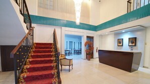 A hotel lobby with a grand staircase, a reception desk, and a seating area.