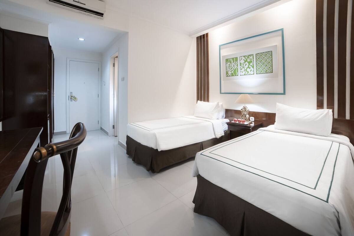 A hotel room with two beds, a desk, a chair, and a wall-mounted artwork.