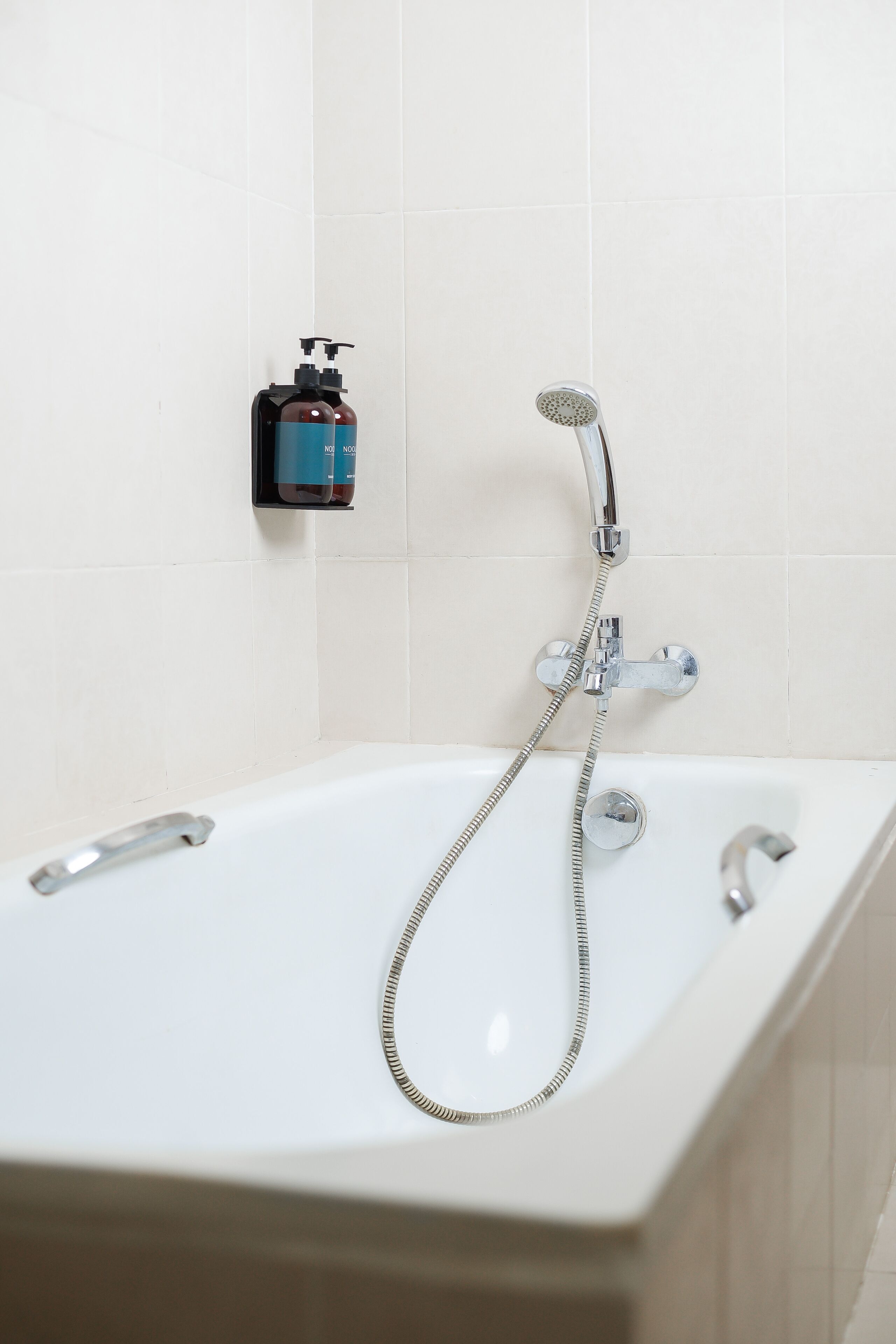 Un baño con una bañera blanca, un cabezal de ducha manual y un dispensador de jabón en la pared.