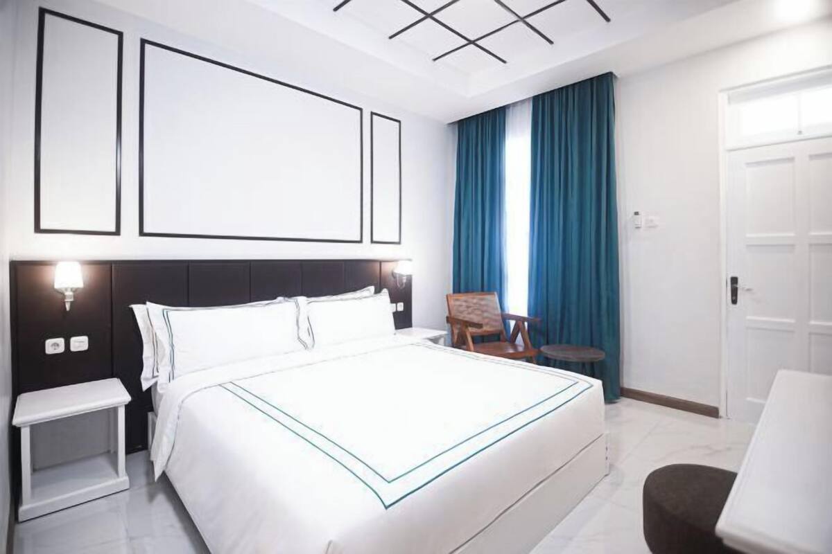 A hotel room with a large bed, bedside tables, a chair, and a small table.
