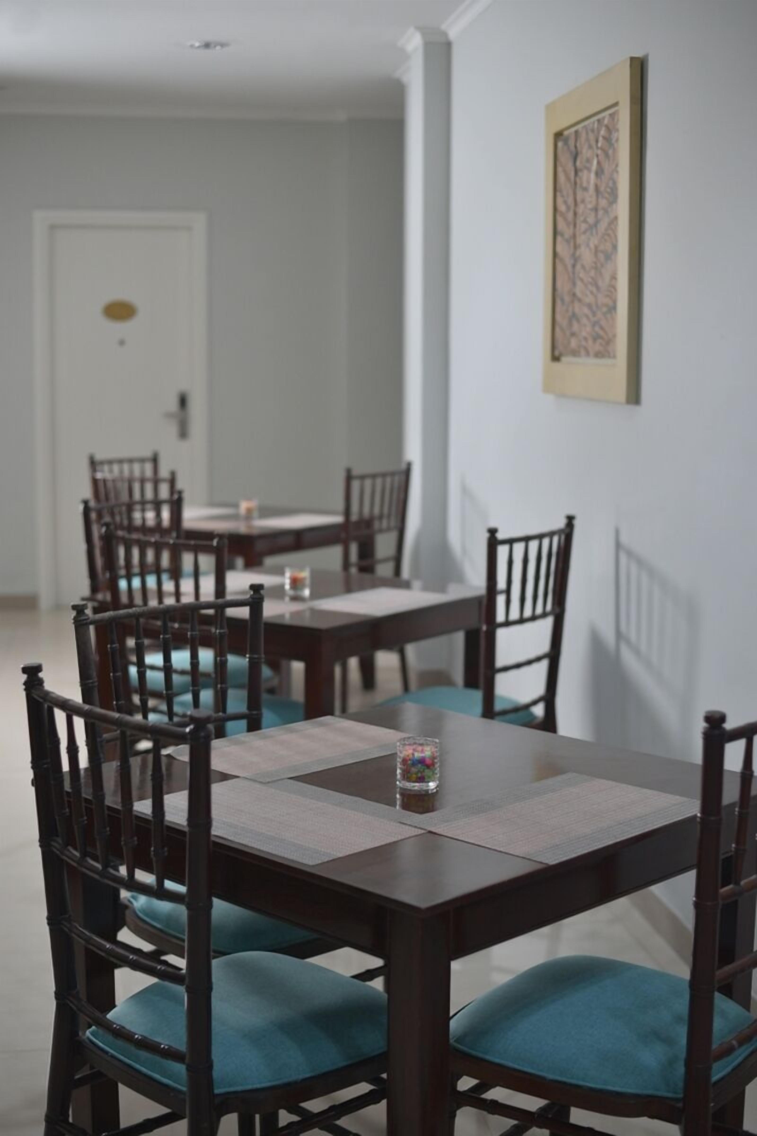 A dining area with multiple tables and chairs, a framed artwork on the wall, and a door in the background.
