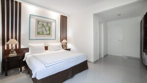 A hotel room with a large bed, two bedside tables with lamps, a framed artwork on the wall, and a door leading to another room.