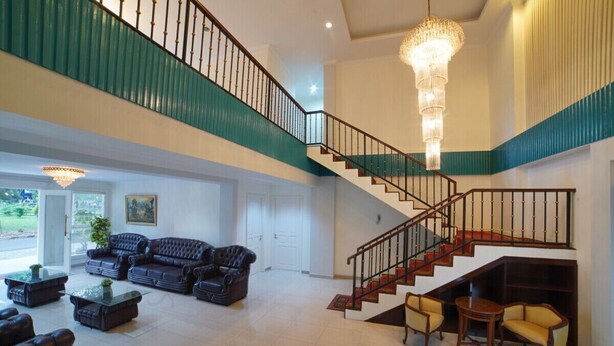 A spacious living area with a staircase, leather sofas, and a chandelier.