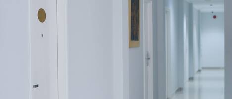 A clean, modern hallway with white walls and a tiled floor, leading to multiple doors.
