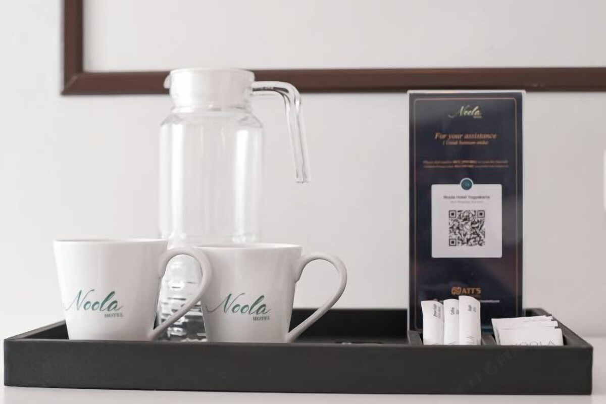 A tray with two white mugs labeled "Noola Hotel," a clear water bottle, and a QR code for hotel services.