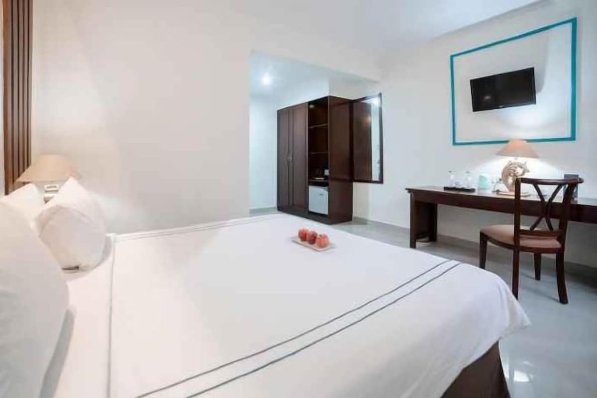 Een hotelkamer met een bed, een bureau, een stoel, een aan de muur bevestigde televisie en een kledingkast.