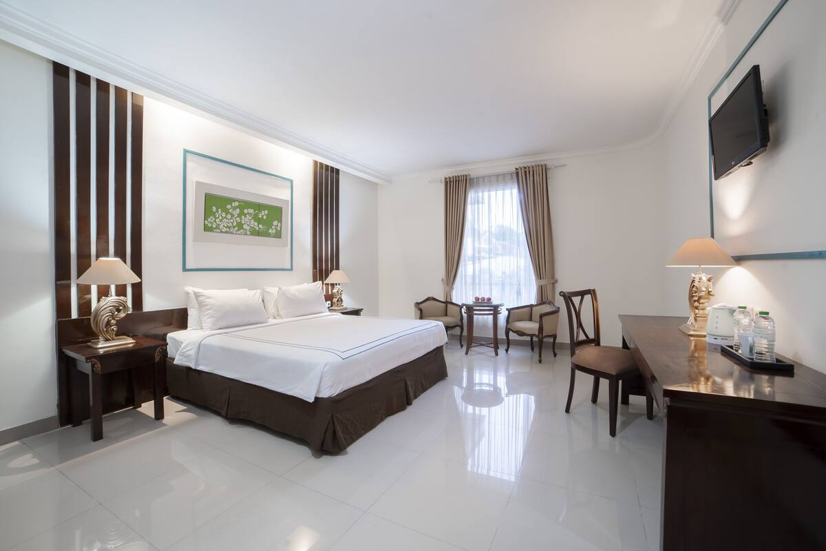 A hotel room with a large bed, a desk, a chair, a small table, a TV, and a picture on the wall.