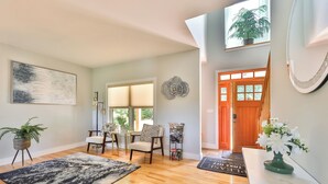 A spacious living room with hardwood flooring, a dining area with two chairs, a large window with blinds, and a door with a decorative flower wall art. - New Luxuary Hunter Ski Resort&Lake Chalet, Hot Tub, Sauna, Fireplace, Mountains (Hunter)