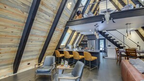 Un loft moderno con techo alto, vigas de madera a la vista, zona de cocina y comedor con taburetes de bar.