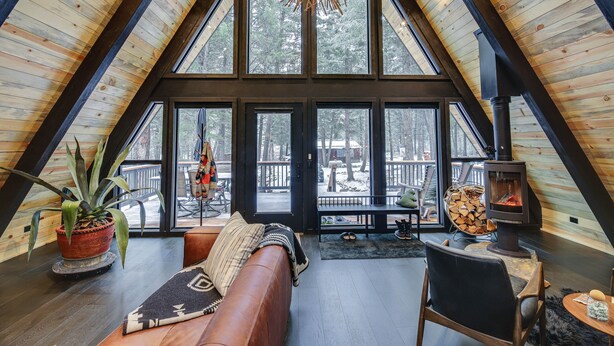 Un acogedor dormitorio tipo loft con techo inclinado, ventanas amplias, techo de madera, chimenea y vistas al exterior.