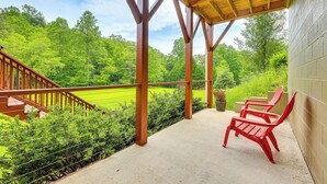 A covered outdoor area with a wooden deck, a concrete floor, and a view of a green field. - Hammocks & Forest Views: Creekside Murphy Retreat (Murphy)