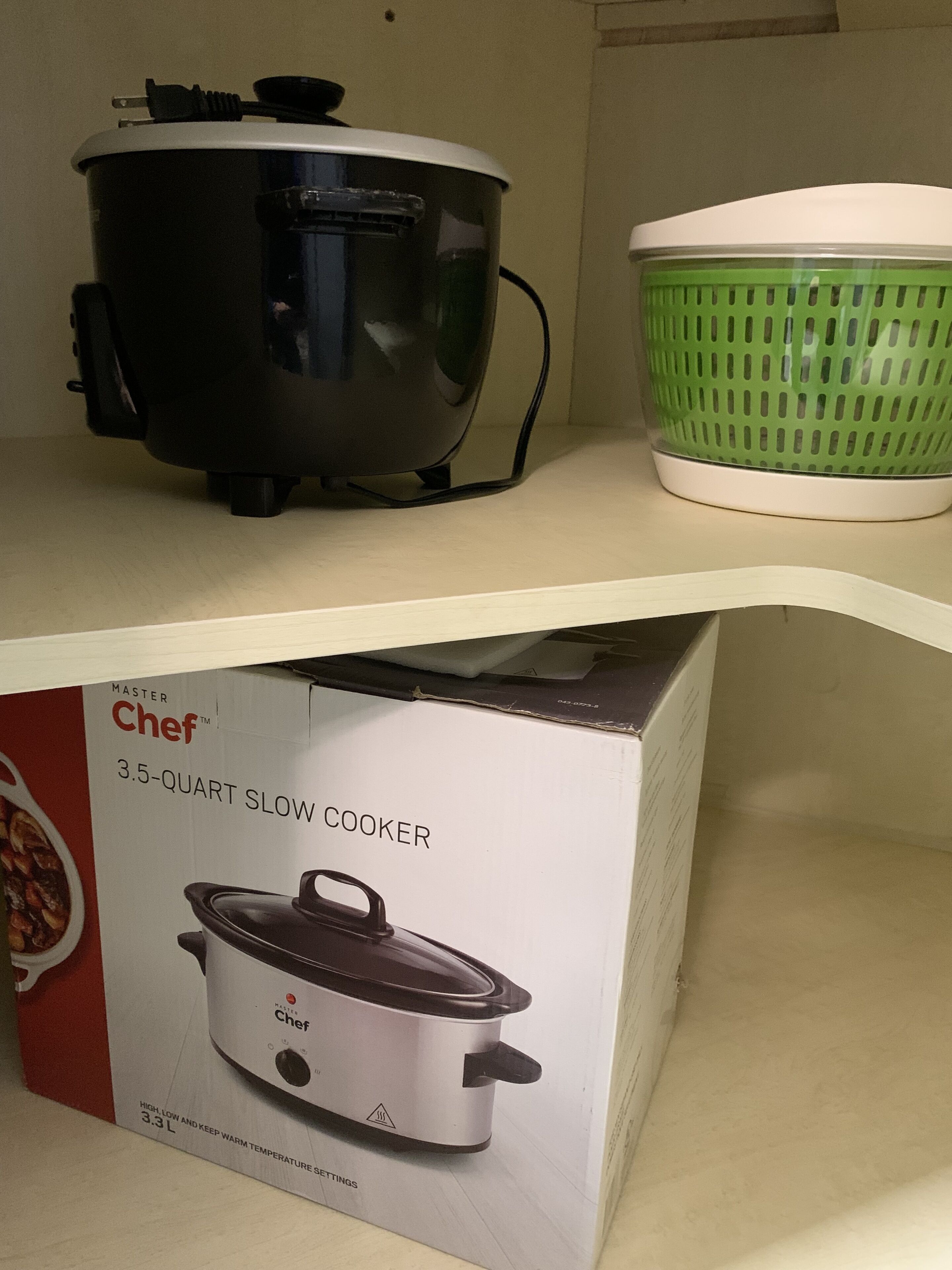 A slow cooker and a green colander on a shelf.