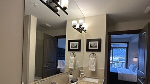 A bathroom with a granite countertop, two sinks, a mirror, and a ceiling light fixture. - Mountain Retreat - Heated Pool & Hot-tub & Sauna (Canmore)