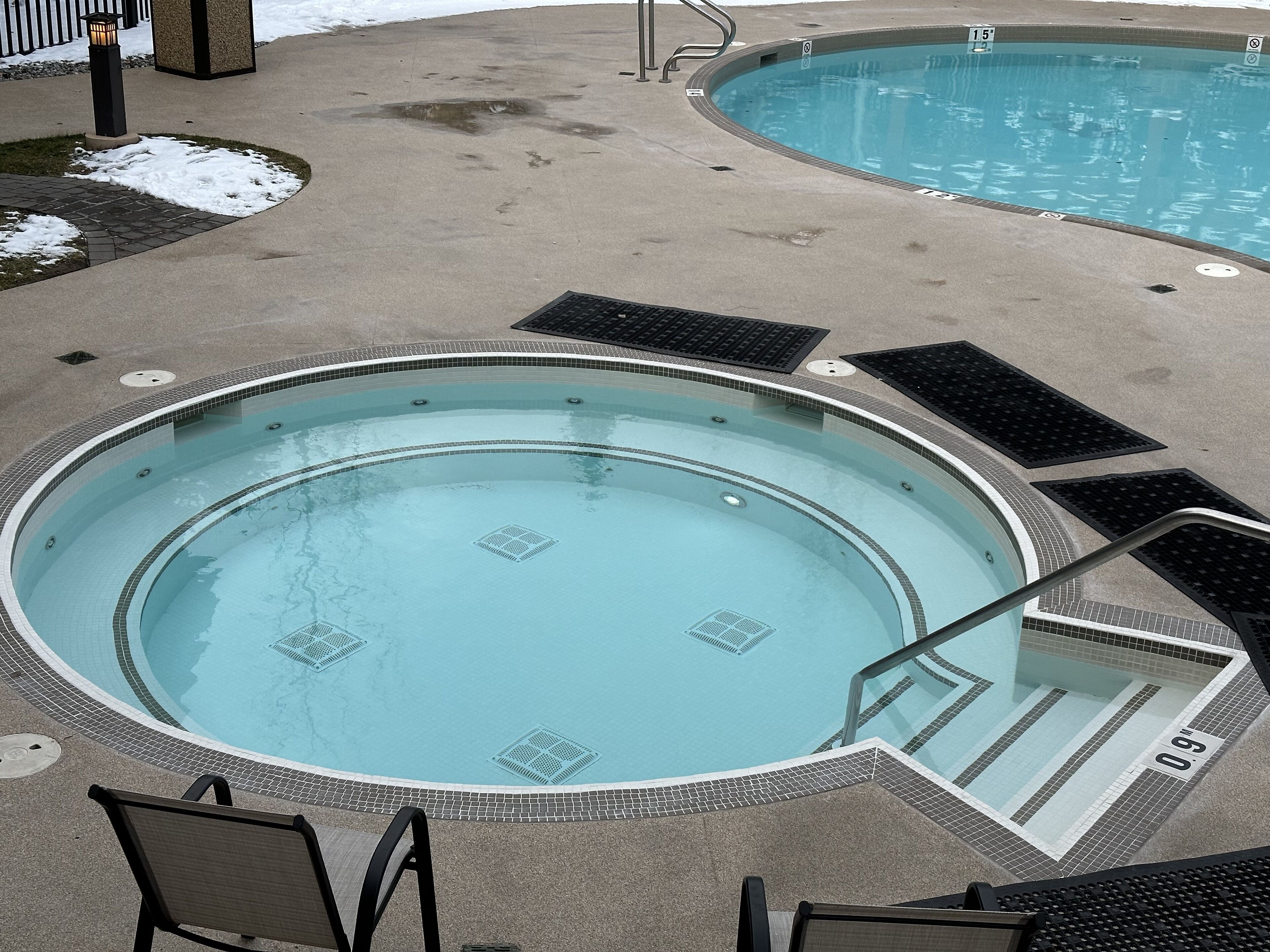 A circular hot tub with a tiled edge, a pool with a tiled edge, and a metal ladder leading into the pool.