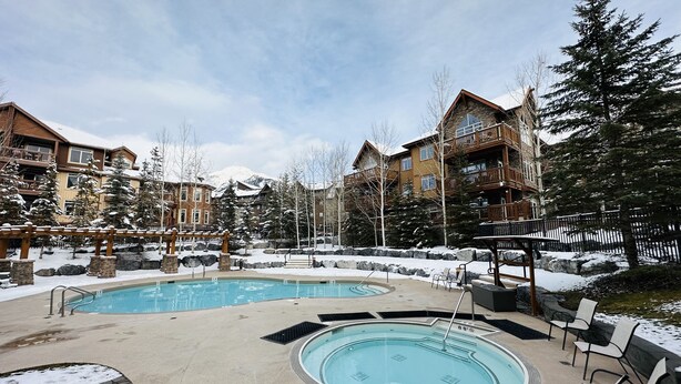 A resort with a pool area, wooden buildings, and snow-covered trees. - Mountain Retreat - Heated Pool & Hot-tub & Sauna (Canmore)