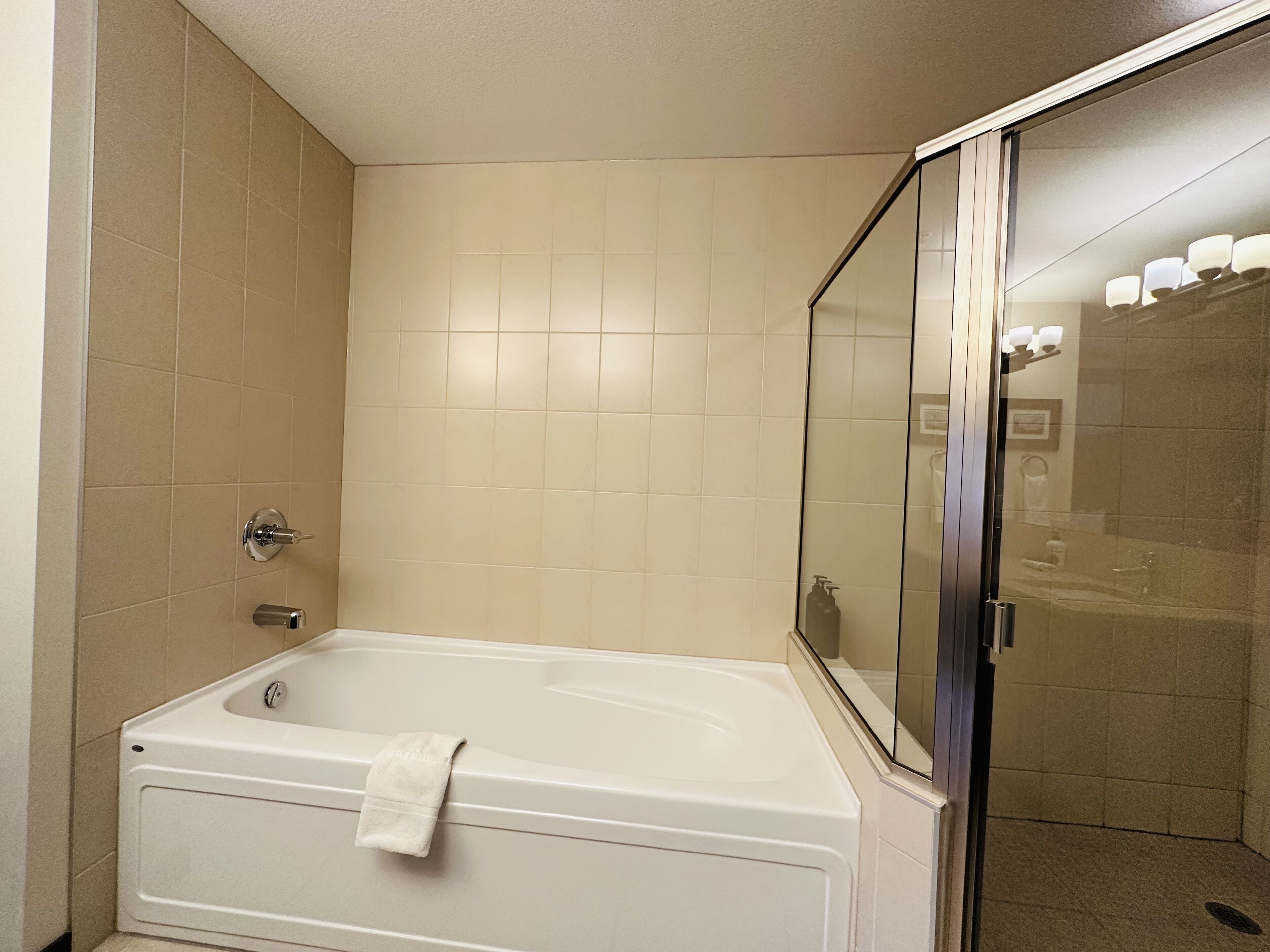 A bathroom with a bathtub, a glass shower enclosure, and beige tiled walls.