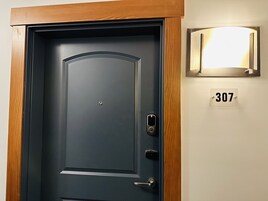 Uma porta escura com fechadura eletrônica, um interfone e uma caixa de correio com o número 307 na parede.