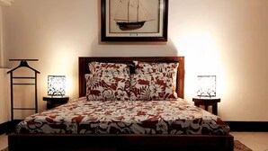 Una cama con colcha estampada, un cuadro enmarcado sobre la cama y dos lámparas de noche.