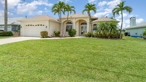 A single-story house with a front yard, palm trees, and a clear sky. - Villa Bonaire: Tranquil Escape w/ Pool & BBQ (Cape Coral)