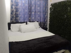 A bed with white bedding and a black headboard, a blue patterned curtain, and a green leafy wall. - Central Sandton Rooms (Sandton)