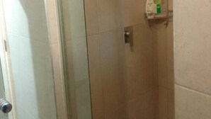 Un espace douche clos par des parois de verre, doté d’un pommeau de douche à main, d’un sol carrelé et d’une étagère pour les articles de toilette.