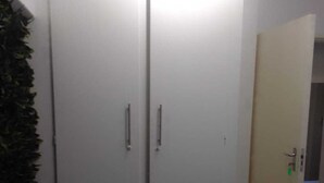 Une pièce avec une armoire fermée, une porte entrouverte et une plante verte sur la gauche.
