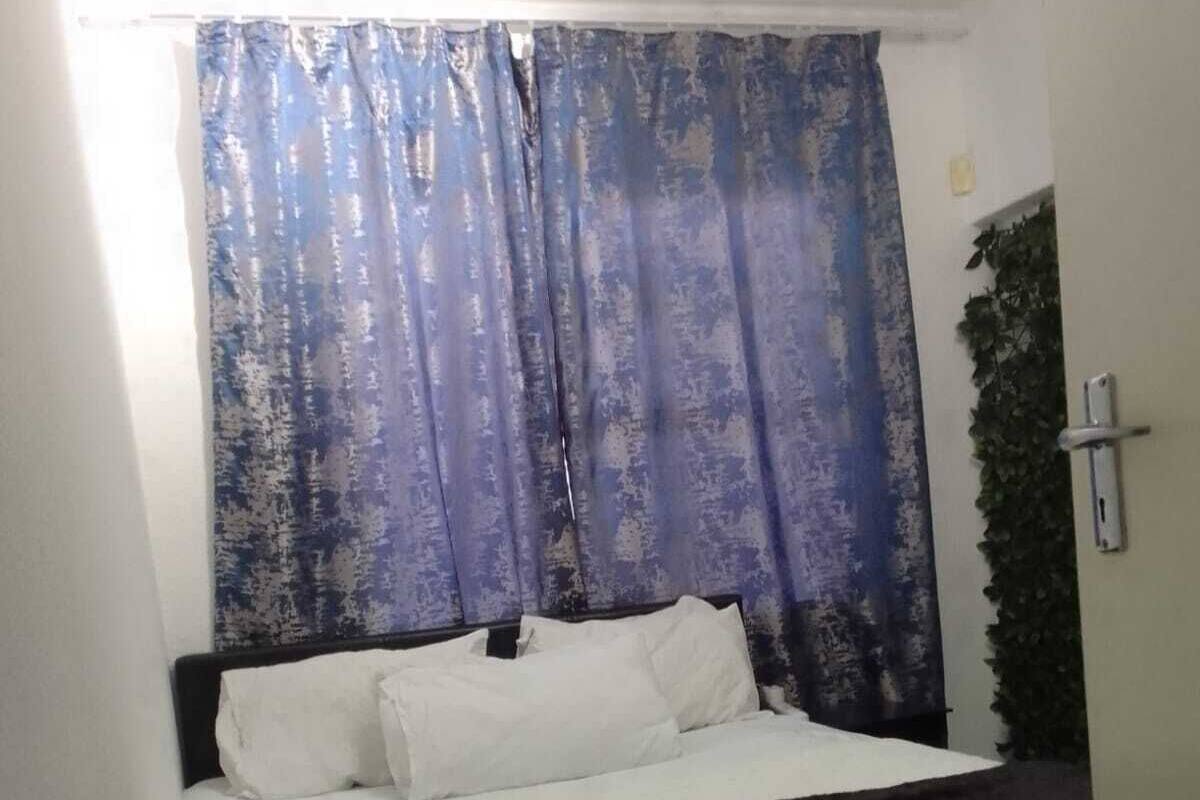 Ein Einzelbett mit weißer Bettwäsche, einem dunklen Kopfteil und einem blauen Vorhang.