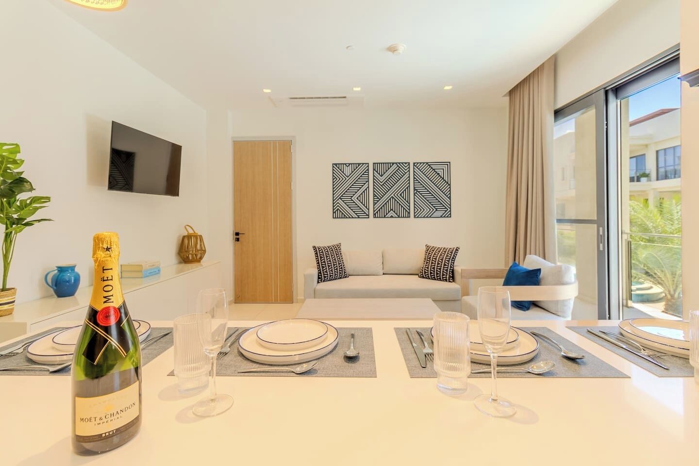 A modern hotel room with a dining area set for a meal, a bottle of Moët & Chandon champagne, and a large window offering a view of the outdoors.